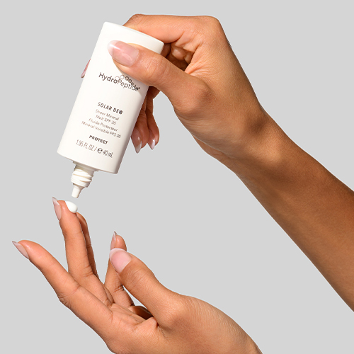 Druppel HydroPeptide Solar Dew zonnebrandcrème die uit de tube op vingers valt