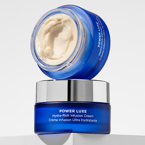 Twee blauwe glazen potten HydroPeptide Power Luxe huidverzorgingscrème op elkaar gestapeld tegen een lichte achtergrond waarvan de bovenste open is.