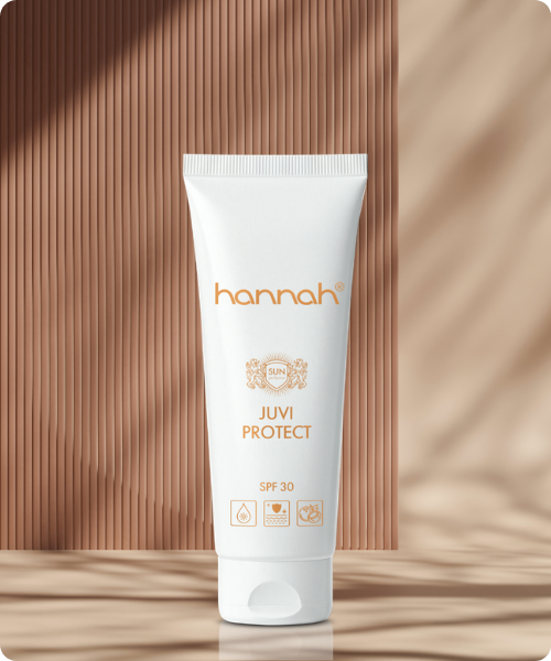 Een witte tube hannah Juvi Protect SPF30 zonnebrandcrème, verticaal gepresenteerd voor een geribbelde bruine wand met invallend zonlicht.
