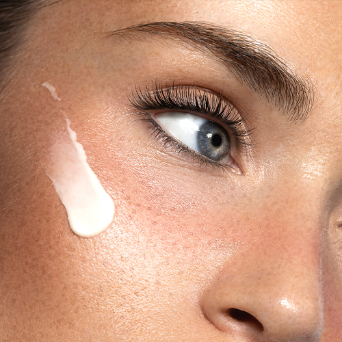 Close-up van de zijdezachte, wit-roze textuur van de EAVE Eye Empower oogcrème op de huid van een model.