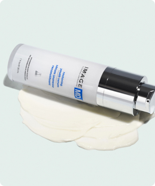 Een flacon IMAGE Skincare IMAGE MD restoring youth serum liggend op een romige, witte serumtextuur.
