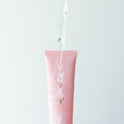 Een roze tube HydroPeptide Daily Drench waar helder water overheen stroomt tegen een lichte achtergrond